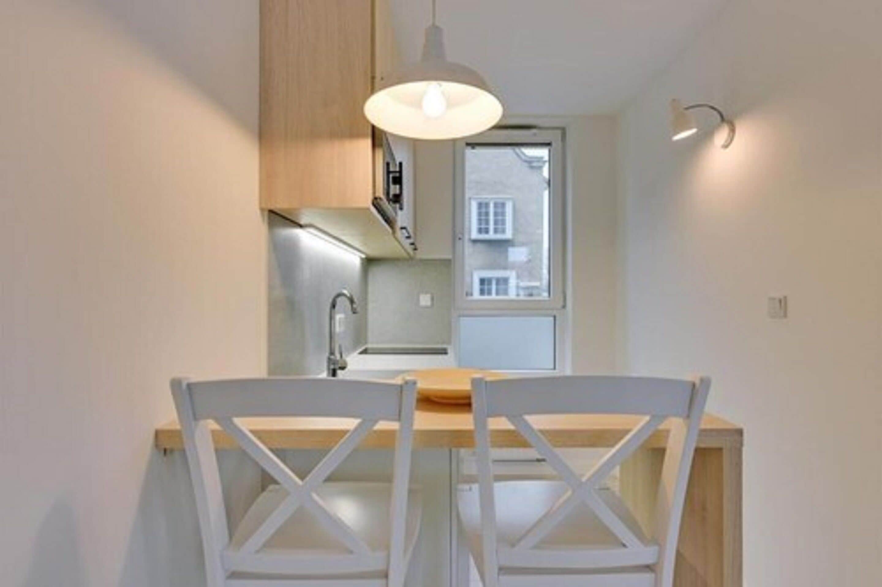 A compact kitchen with white cabinetry, a wooden countertop, and a hanging pendant light.