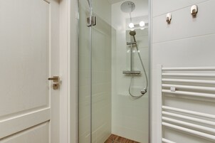 A modern bathroom with a glass shower enclosure, a white tiled wall, and a white towel rack.