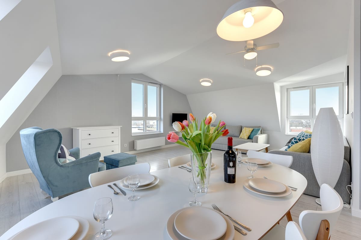 Un coin repas moderne avec une table blanche dressée pour quatre personnes, un vase de tulipes et une bouteille de vin.