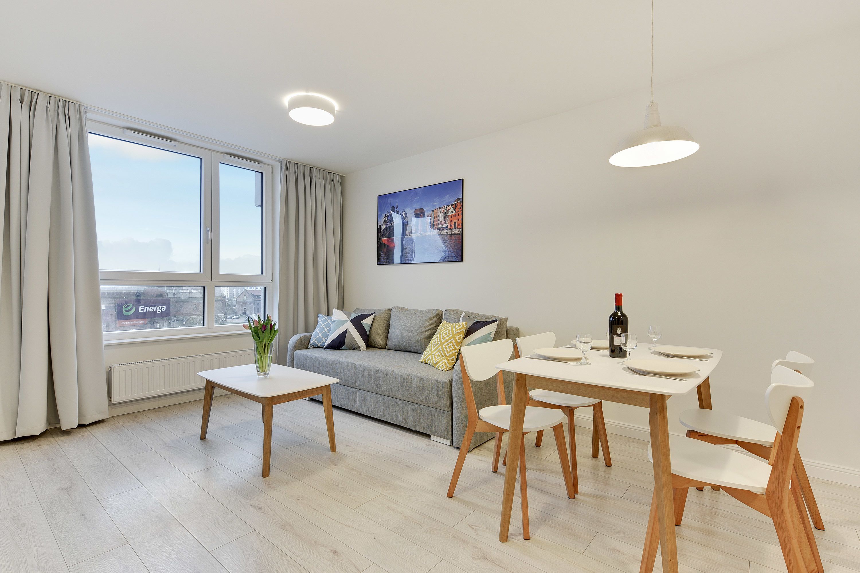 Een moderne woonkamer met een bank, eettafel en stoelen. Er is een raam met gordijnen te zien, en een schilderij hangt aan de muur.