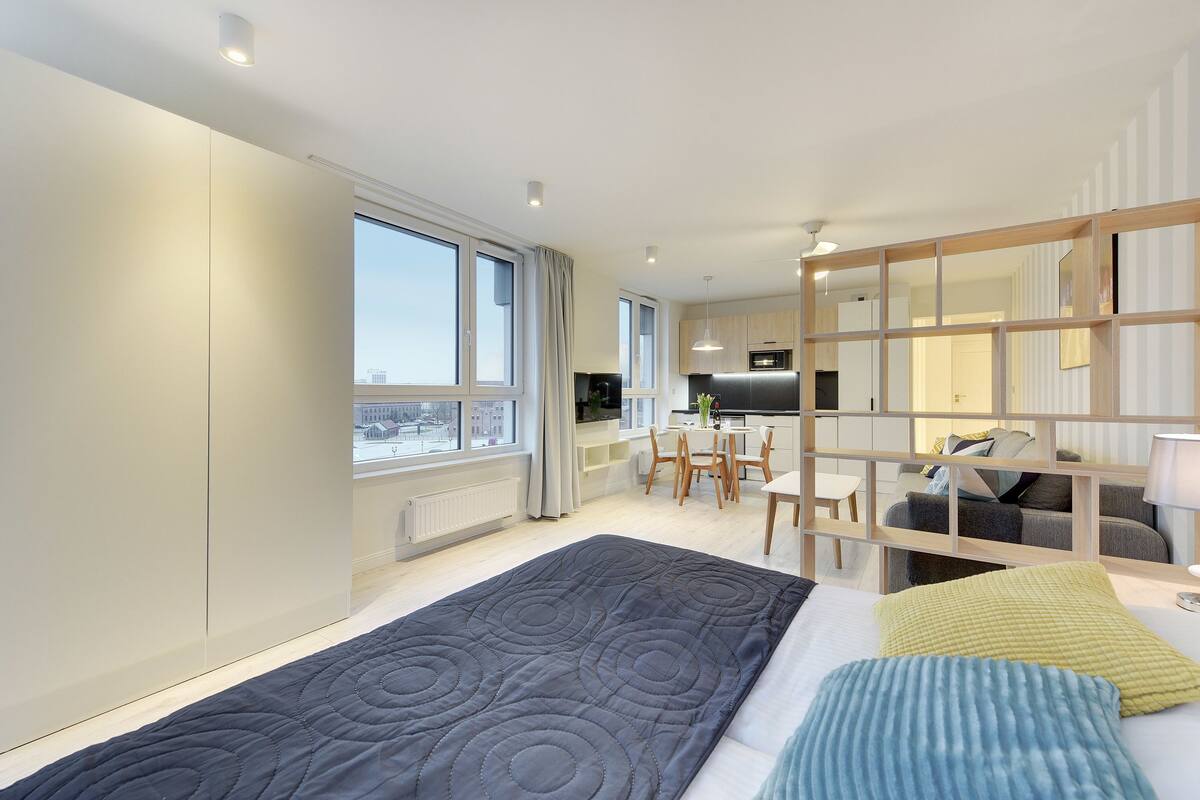 Une chambre d’hôtel moderne avec un grand lit, un coin repas et une cuisine en arrière-plan.