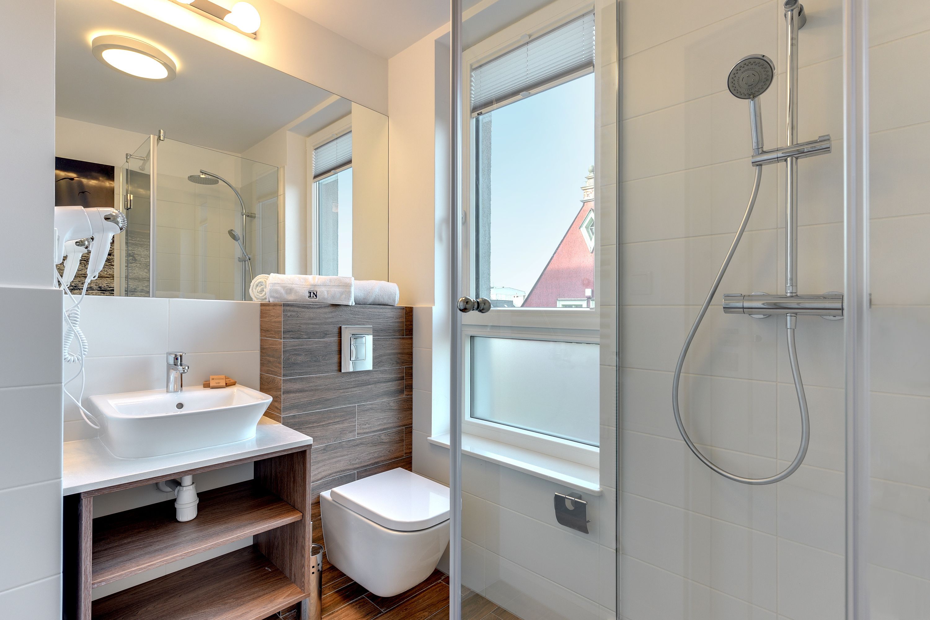 A modern bathroom with a white sink, a toilet, a glass-enclosed shower, and a large mirror.