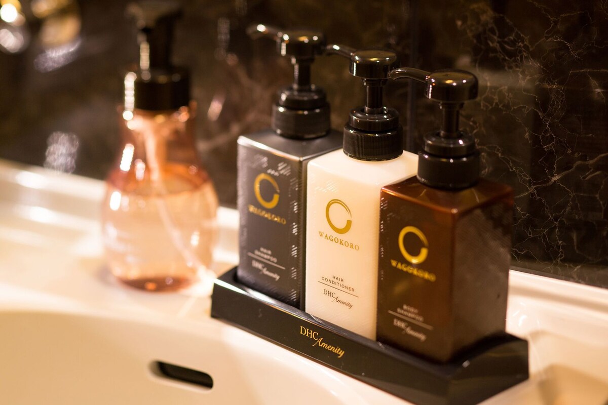 Un baño con lavamanos de mármol y tres productos para el cabello en un dispensador negro.