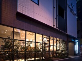 Exterior de un hotel con grandes ventanales, un restaurante visible llamado "GREENBOWL" y un cartel que dice "TOSEI HOTEL COCONE".