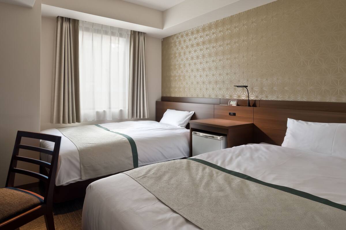 Een hotelkamer met twee bedden, een houten nachtkastje, een bureau, een stoel en een raam met gordijnen.