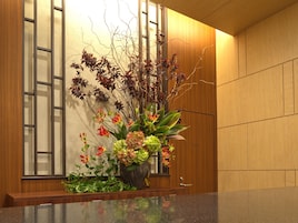 Un área de recepción con un mostrador de madera, un jarrón grande con flores y una pared de madera con paneles verticales.