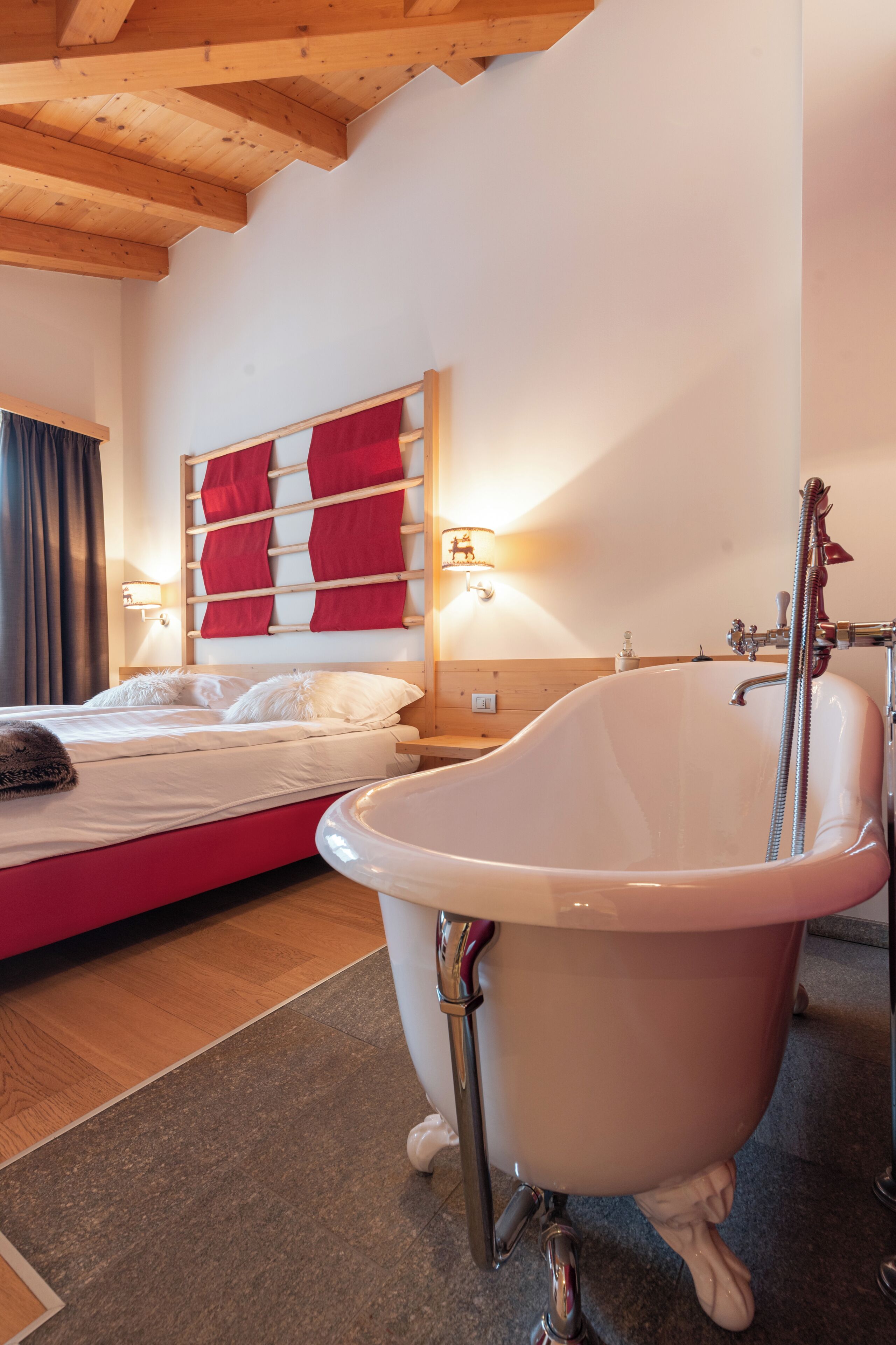 A bedroom with a large bathtub, a bed with white bedding, a wooden headboard, and a wall-mounted light fixture.