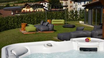 Un jacuzzi con cubierta de madera, asientos exteriores y vistas a casas al fondo.
