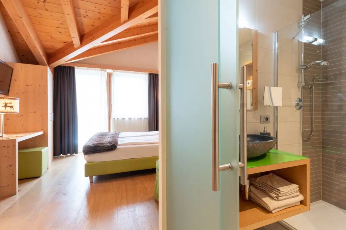 A modern bedroom with a bed, a bedside table, a window, and a bathroom with a shower and sink.