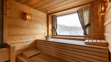 Interior de una cabaña de madera con un banco, una ventana con cortinas y una mesita con un hervidor.