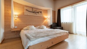 A bedroom with a wooden bed, two bedside lamps, a branch artwork on the wall, and a large window with curtains.