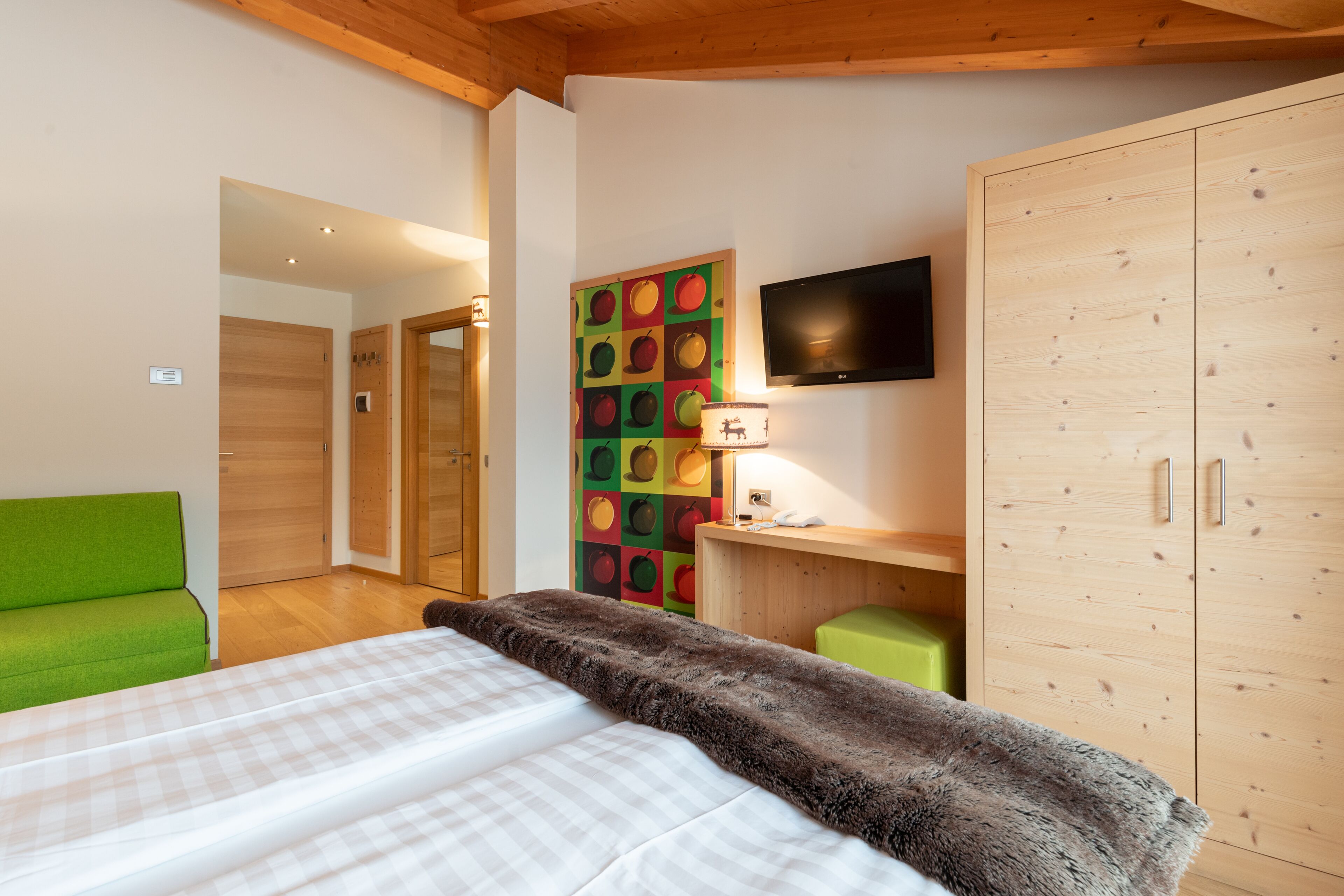Una habitación de hotel con una cama, un sofá verde, un armario de madera, un televisor y un adorno de pared colorido.