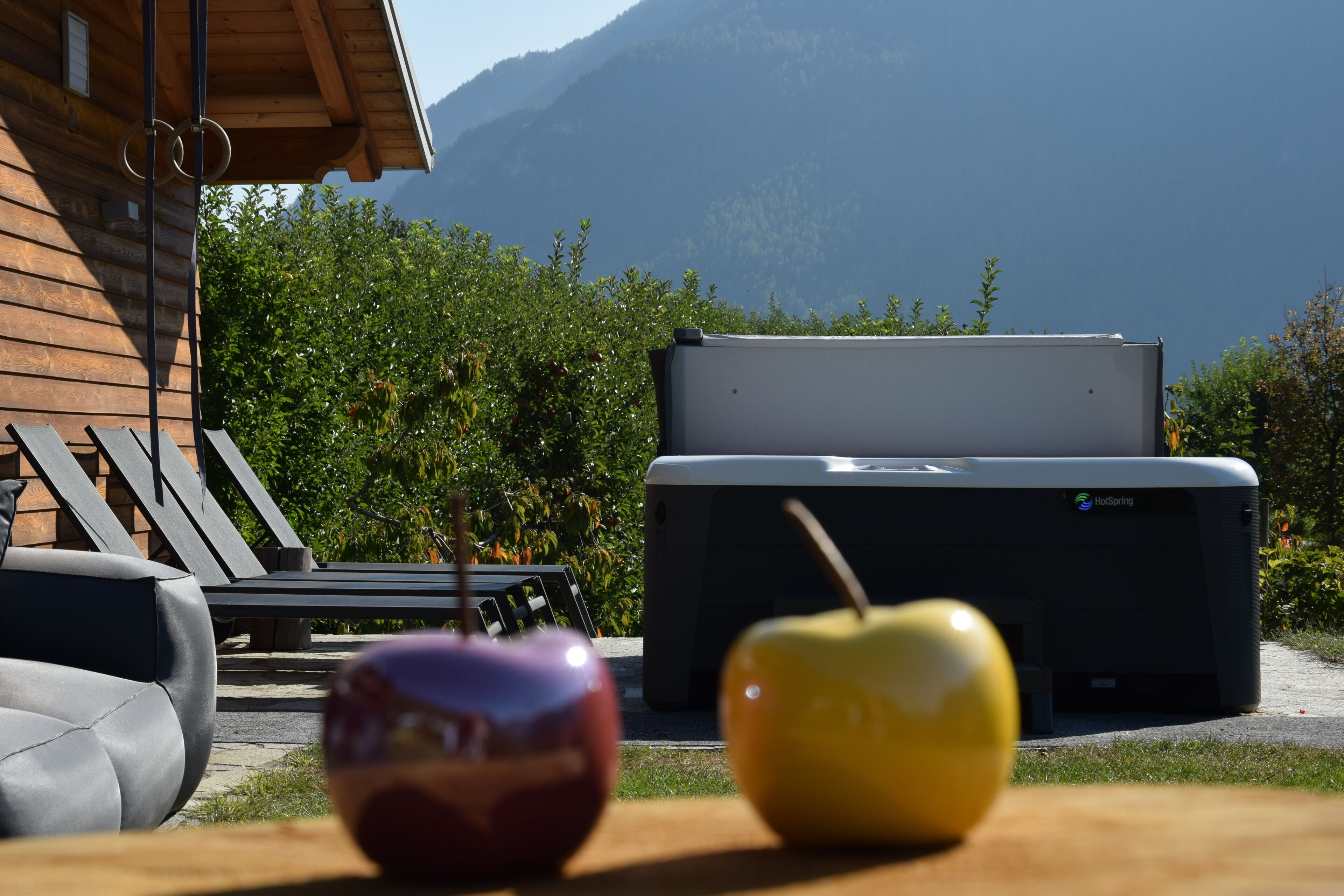 Una cabaña de madera con aguas termales, dos manzanas sobre una mesa y una montaña al fondo.