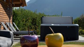 Una cabaña de madera con aguas termales, dos manzanas sobre una mesa y una montaña al fondo.