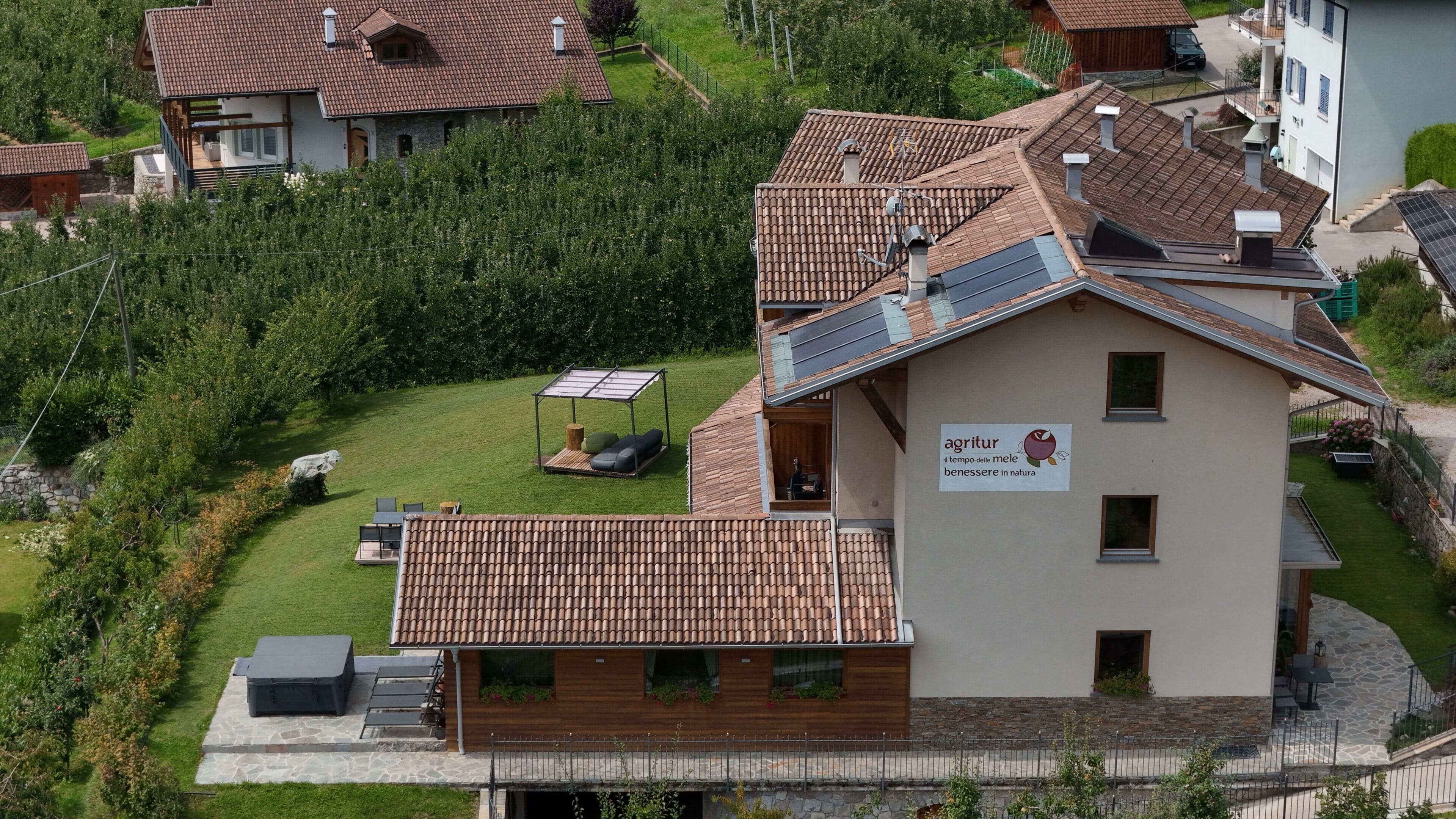 Un immeuble à plusieurs étages, doté d’un toit en tuiles, d’une enseigne indiquant une orientation vers la nature et le bien-être, et d’une pelouse bien entretenue avec des espaces de repos extérieurs.
