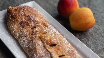 Een lang, rechthoekig gebakje bestrooid met poedersuiker, geserveerd met twee stukken fruit op een bord.