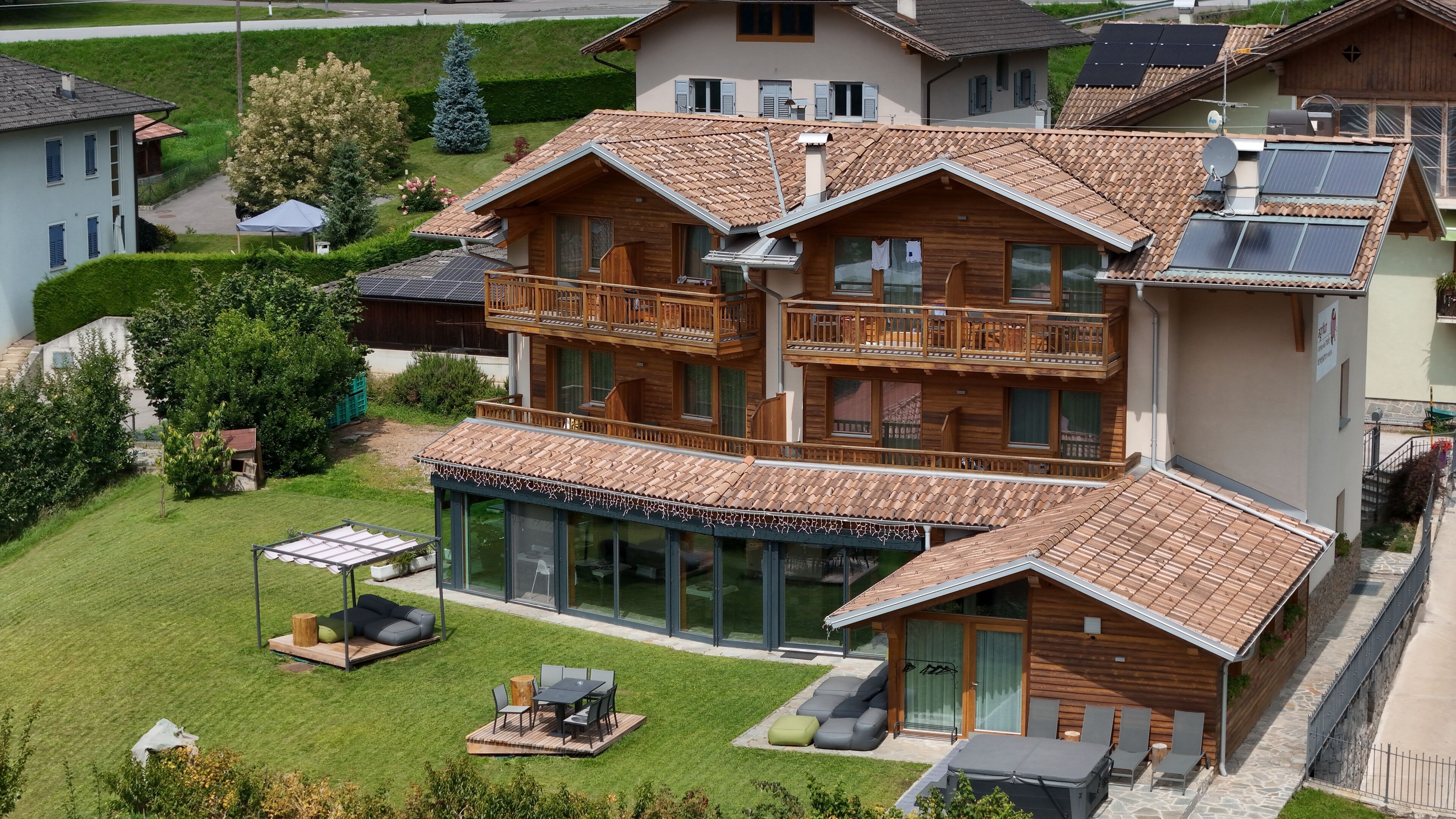 Una casa a più piani in legno con un balcone, una veranda in vetro e un prato curato.