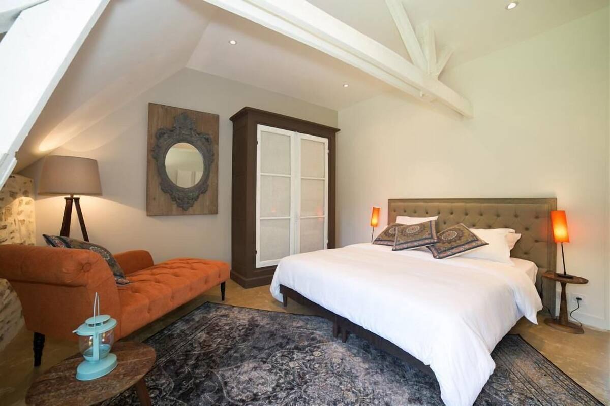 Un dormitorio con cama, sofá, lámpara, espejo y ventana.
