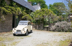 A vintage car parked in front of a stone building with a garden.