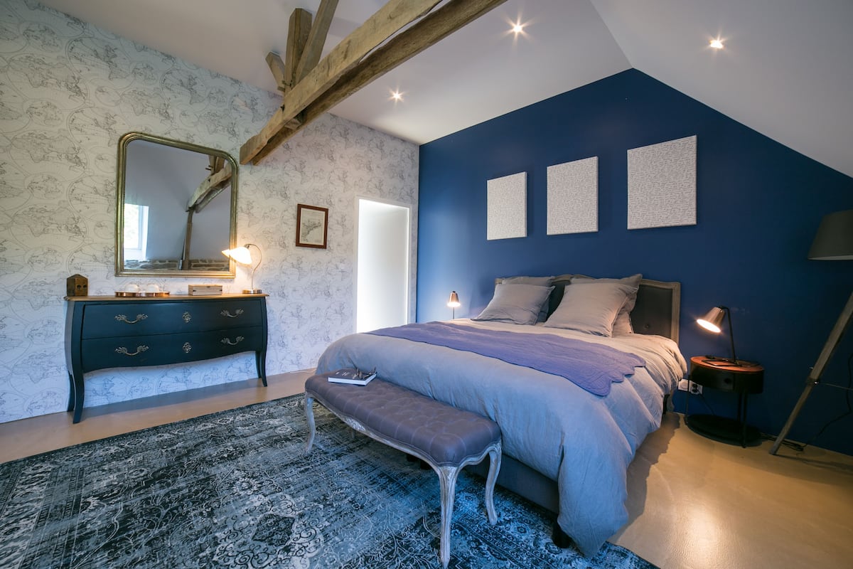 Un dormitorio con una cama grande, un aparador, un banco, un espejo y tres cuadros en la pared.