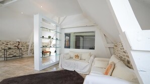 Quarto estilo loft moderno com uma janela grande, uma estante de vidro, um sofá branco e um tapete escuro.