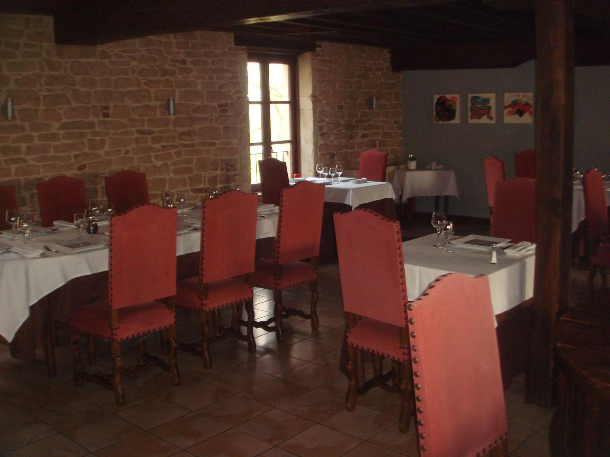 Un espace repas avec des murs en pierre, des chaises à revêtement rouge et des nappes blanches.