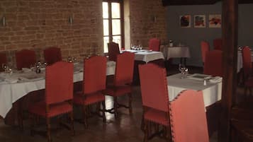 Un espace repas avec des murs en pierre, des chaises à revêtement rouge et des nappes blanches.