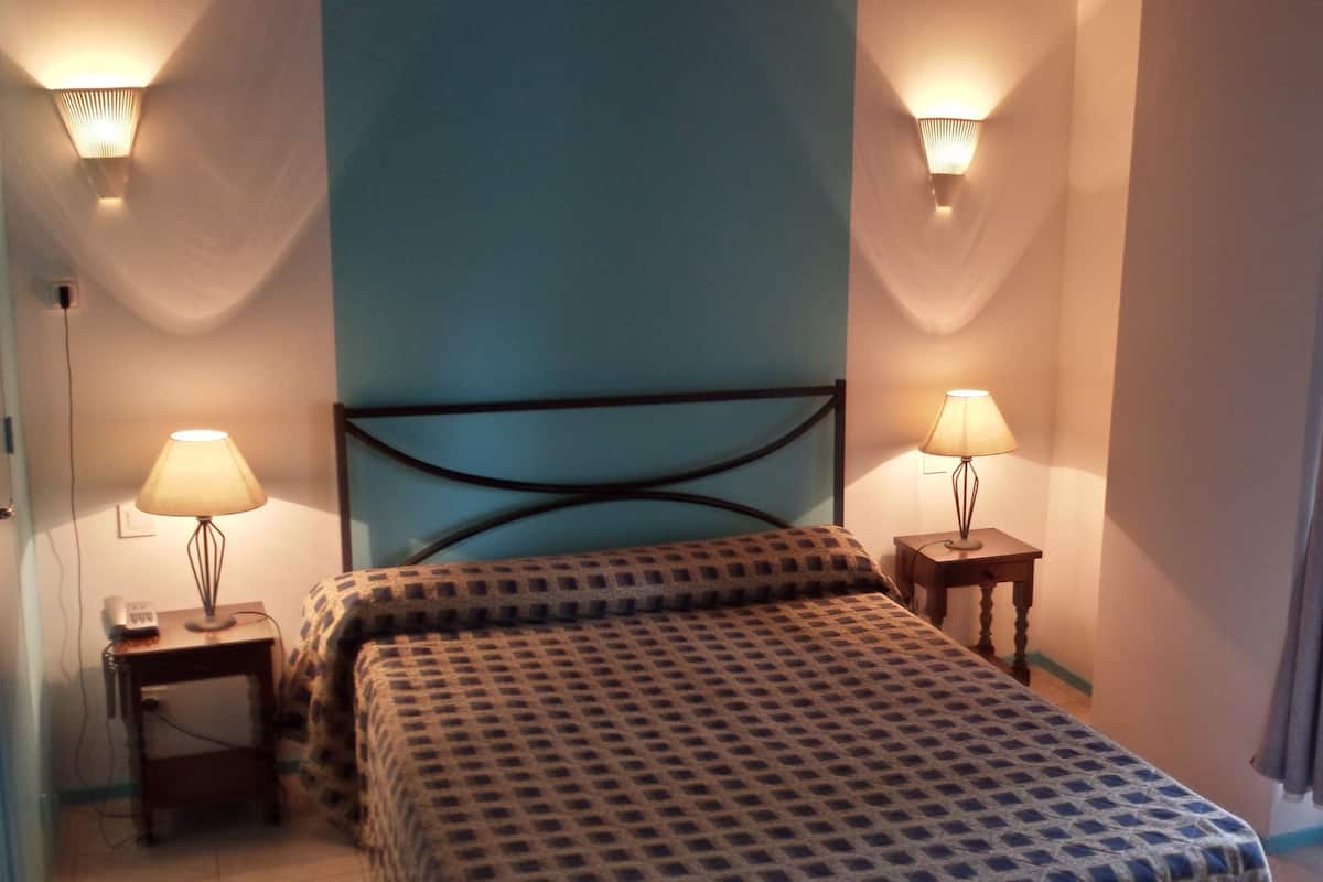 Ein Schlafzimmer mit einem Bett, zwei Nachttischen, einer Wandlampe und einem Fenster mit Vorhängen.