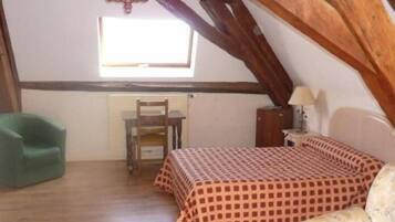 Ein kleiner, gemütlicher Raum mit schragem Dach, einem Einzelbett mit karierter Bettdecke, einem grünen Sessel, einem kleinen Tisch und einem Fenster, das natürliches Licht hereinlässt.