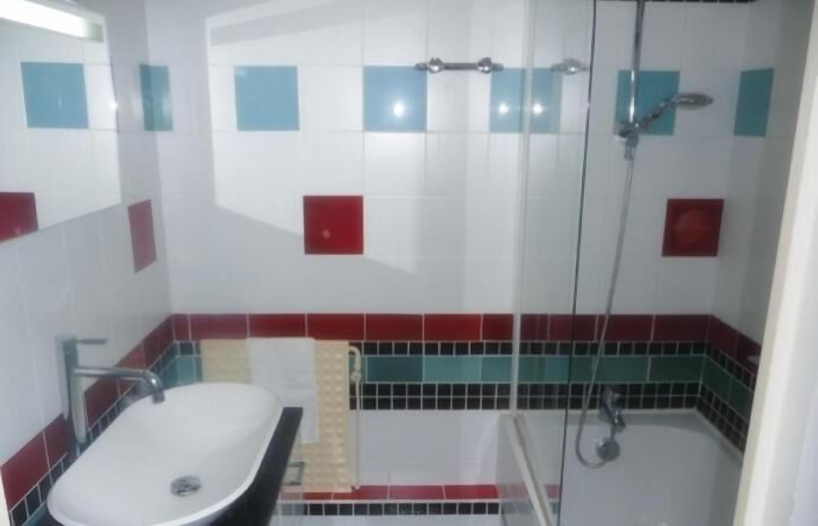 Een badkamer met een wit wastafelmeubel, een douche en betegelde muren met rode en blauwe accenten.