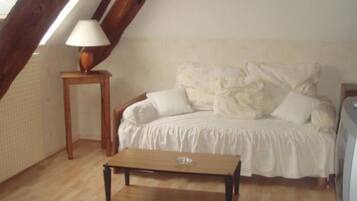 Una habitación acogedora con techo de madera, una cama con ropa de cama blanca, una pequeña mesa de madera con una lámpara y piso de baldosas.