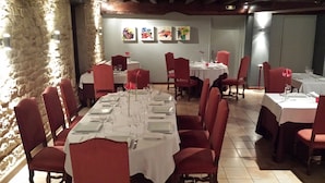 Un restaurant avec une longue table dressée pour le dîner, des chaises rouges et des œuvres d’art accrochées au mur.