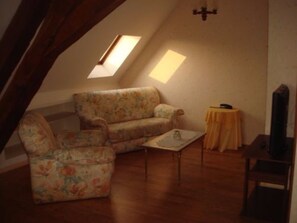 Un cuarto ático acogedor con un sofá floral, una pequeña mesa y un televisor.