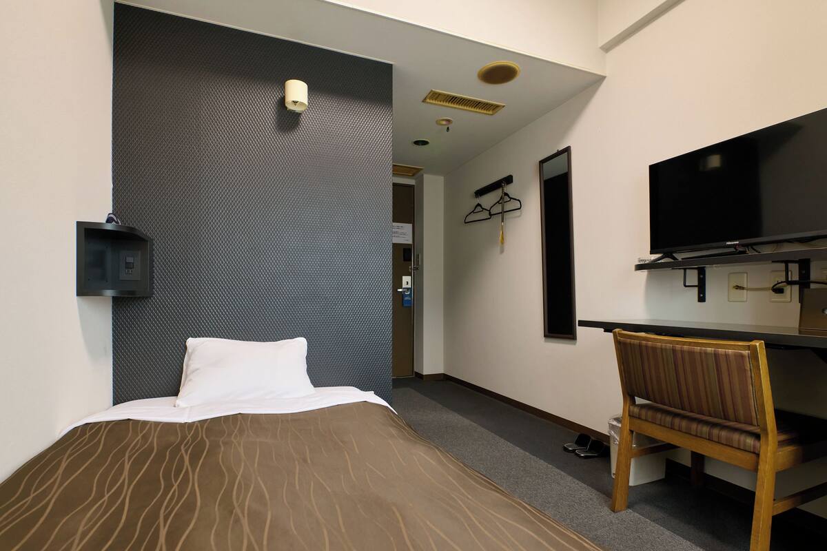 Hotellihuone, jossa on sänky, työpöytä, tuoli, televisio ja seinään kiinnitetty valaisin.