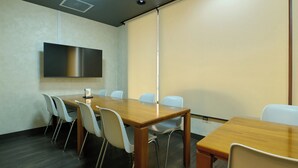 A conference room with a long table and chairs, a flat-screen TV, and a projector screen. - Hotel Seishokan (Shizuoka)