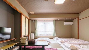 A traditional Japanese-style room with tatami flooring, a television, a small table, and two beds. - Hotel Seishokan (Shizuoka)