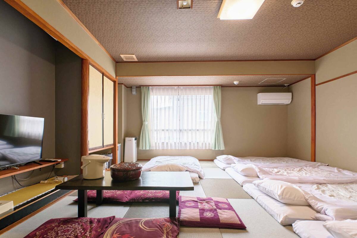 Perinteinen japanilaistyylinen huone, jossa on tatamimatto, televisio, pieni pöytä ja kaksi sänkyä.
