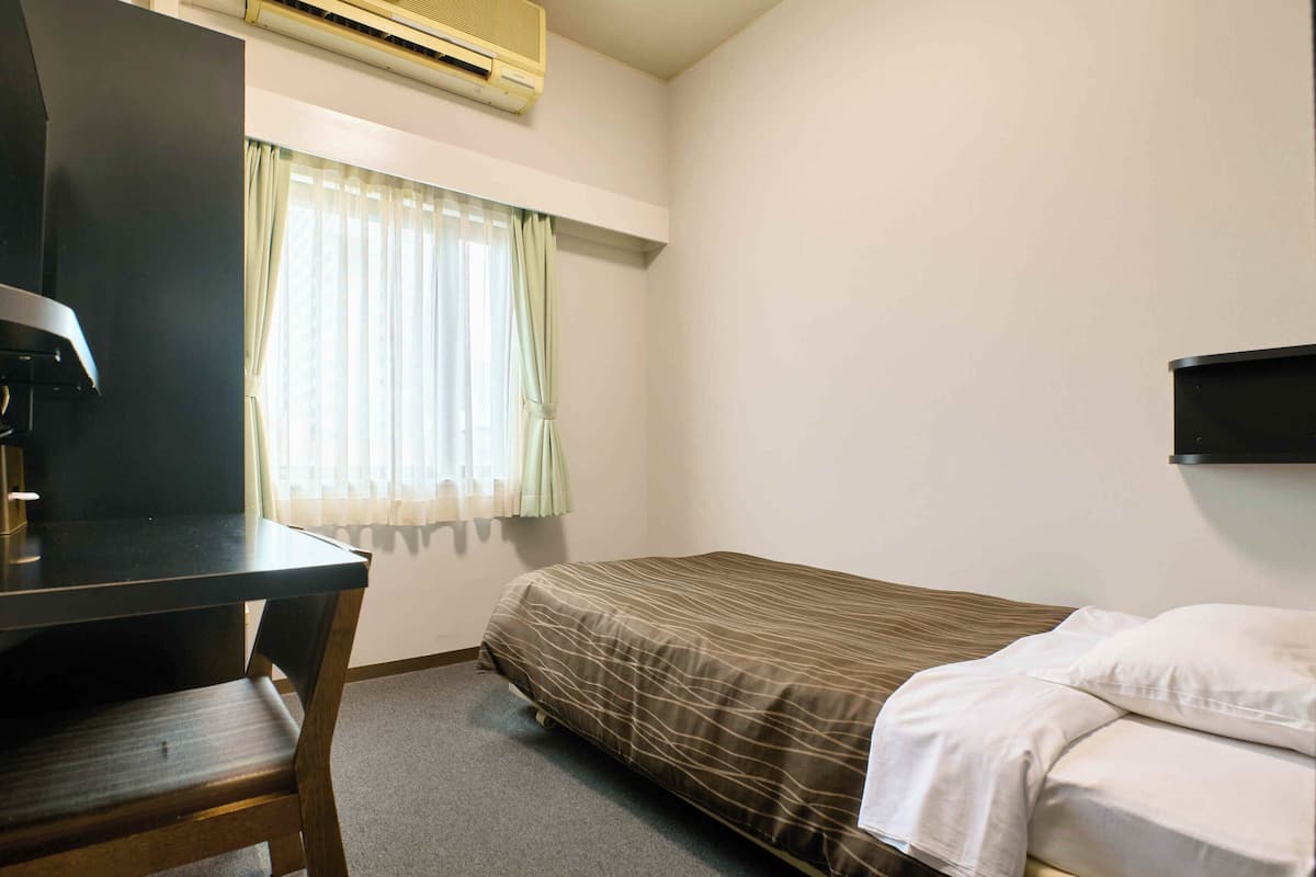 Pieni hotellihuone, jossa on yksi huone, sänky, työpöytä ja tuoli.
