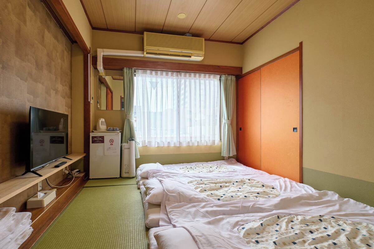 Hotellihuone, jossa on kaksi sänkyä, televisio, jääkaappi ja ikkuna, jossa on verhot.