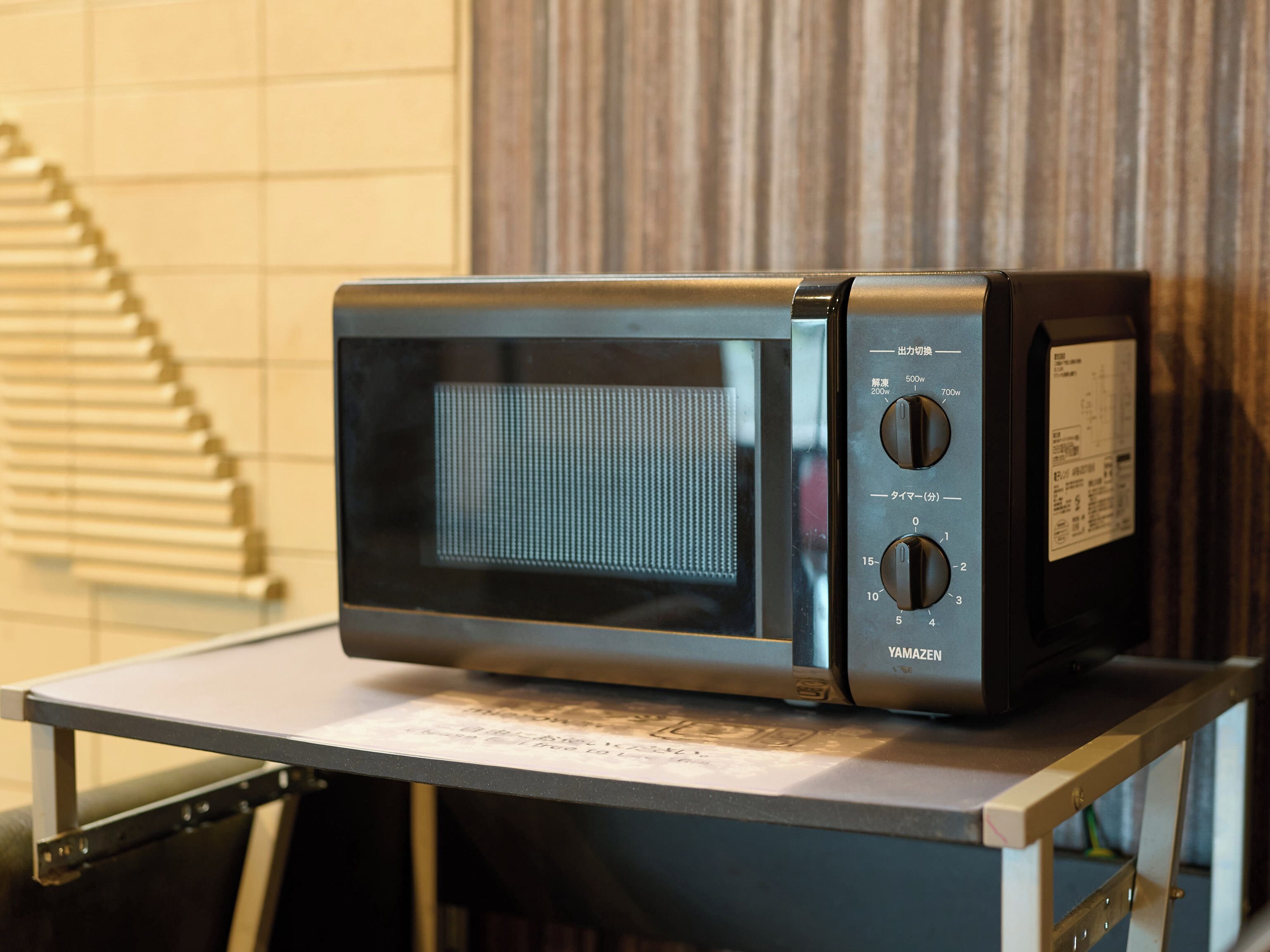 A black microwave on a metal cart with a label underneath.