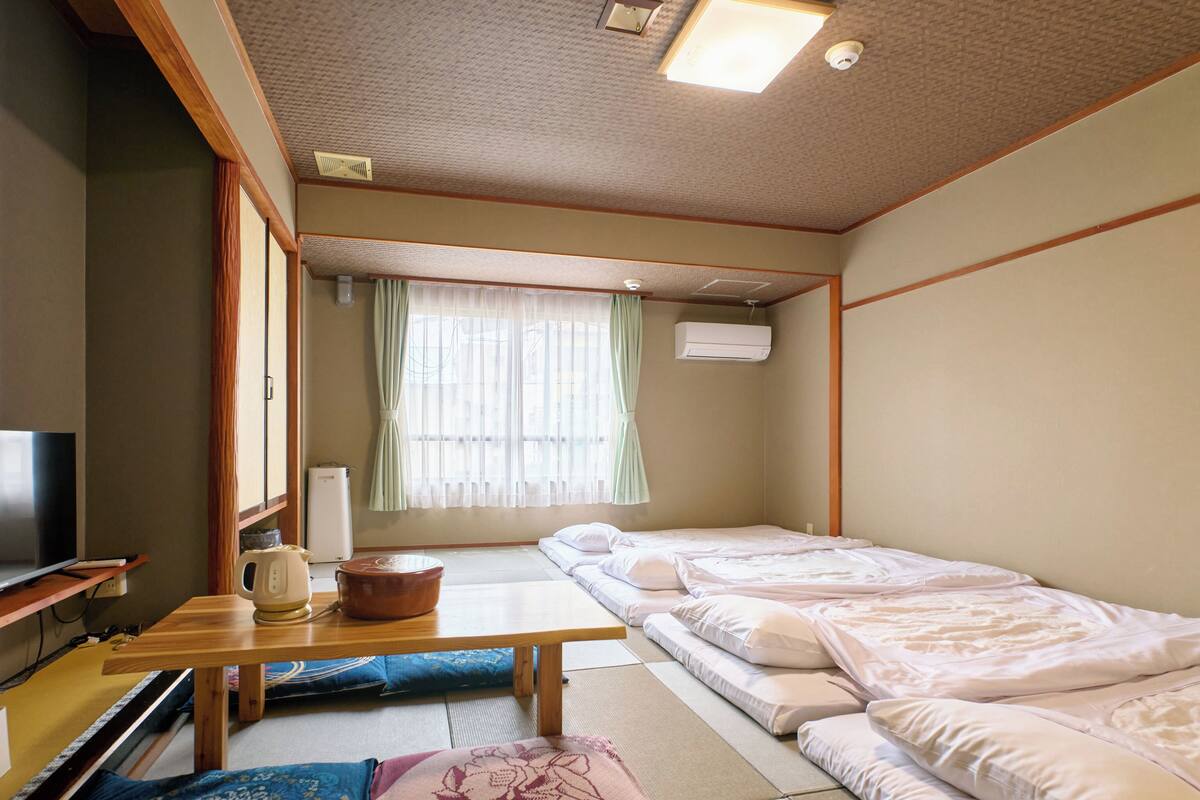 Perinteinen japanilaistyylinen huone, jossa on tatamimatto, futon-patja, televisio sekä pieni pöytä, jossa on vedenkeitin ja kuppeja.