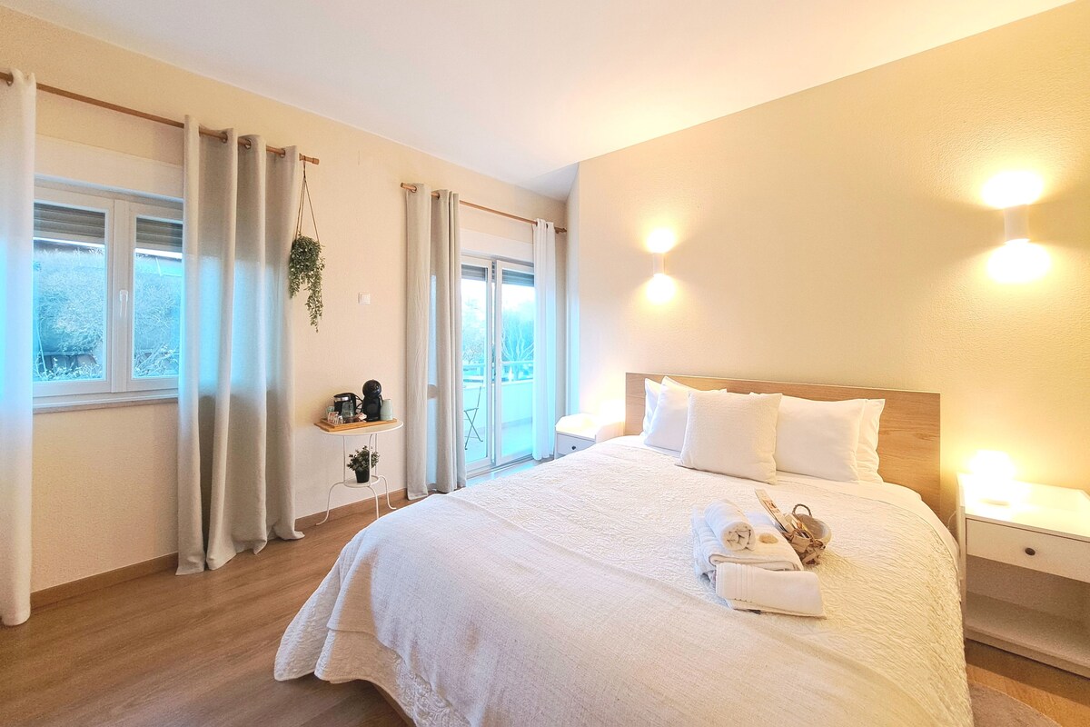 Une chambre à coucher avec un grand lit, des tables de chevet, une fenêtre avec des rideaux et une vue sur l’extérieur.