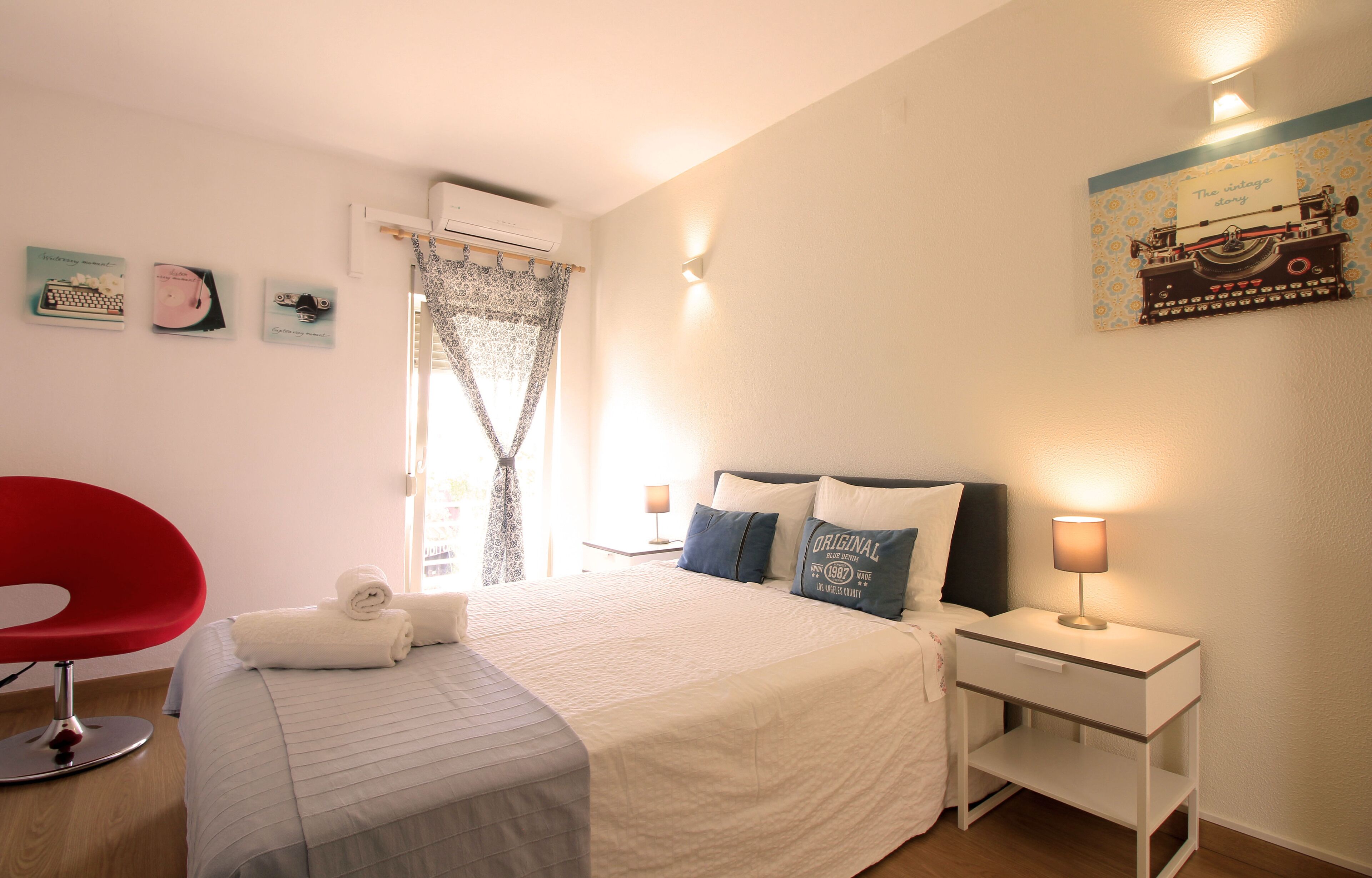 A neatly arranged bedroom with a bed, bedside tables, a red chair, and wall decorations.