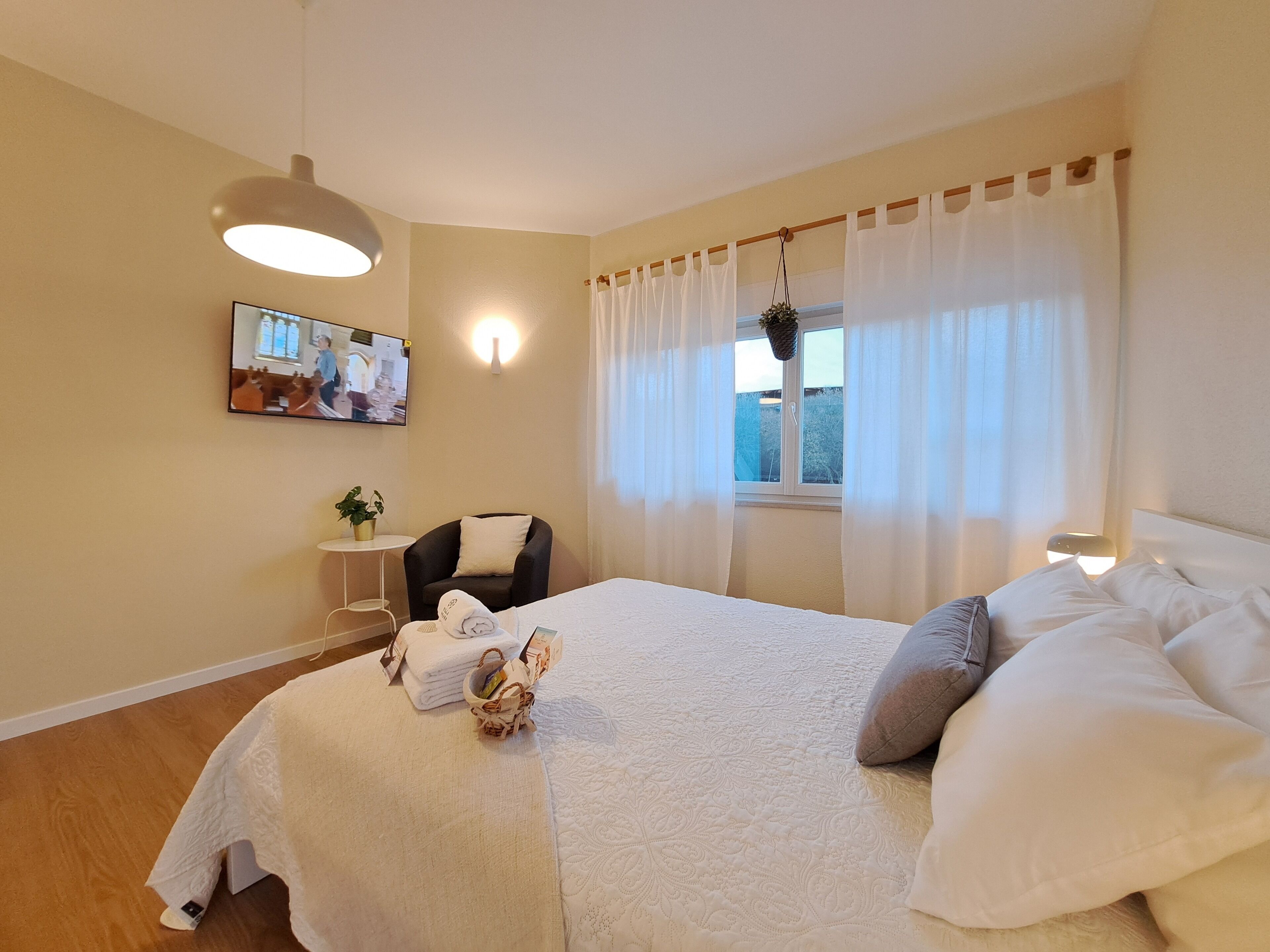 Ein Schlafzimmer mit einem Bett, einem Sessel, einem kleinen Tisch mit einer Pflanze und einem Bild an der Wand.