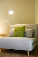 Un sofá gris con un cojín verde y una lámpara de pie en una habitación con suelo de madera.