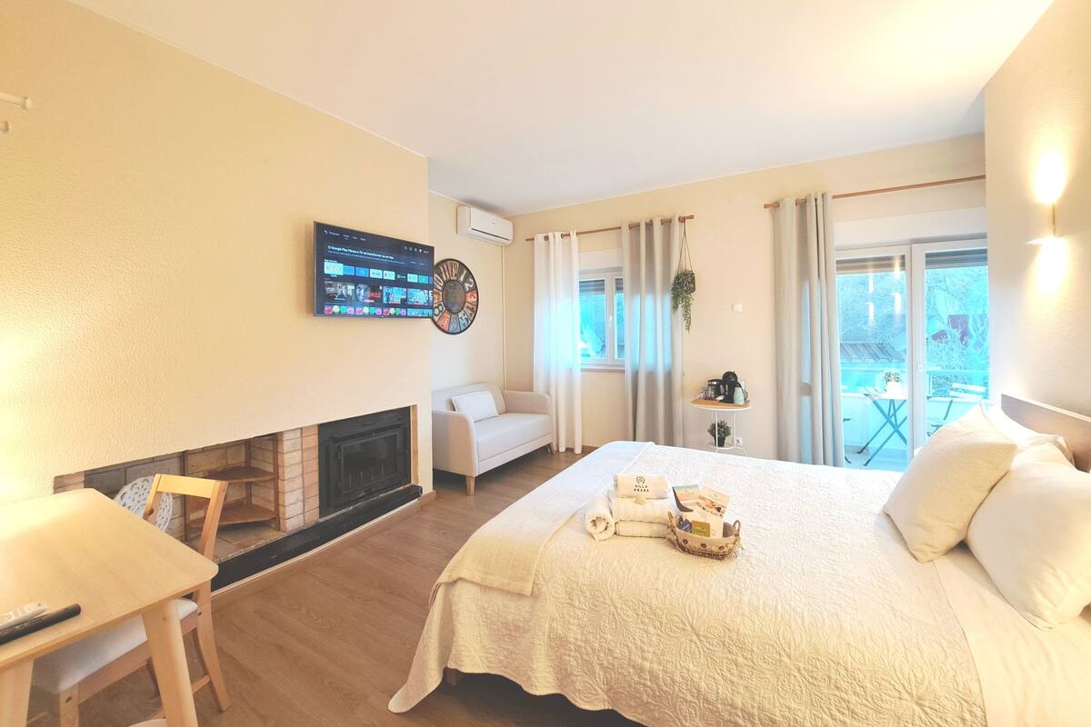 Ein Hotelzimmer mit Bett, Wandfernseher, Kamin, Sofa und Balkon mit Tisch und Stühlen.