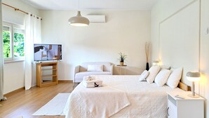 A modern bedroom with a large bed, a TV, a small side table, and a bedside lamp. - Villa Prana Guesthouse, Yoga & Ayurveda (Portimão)
