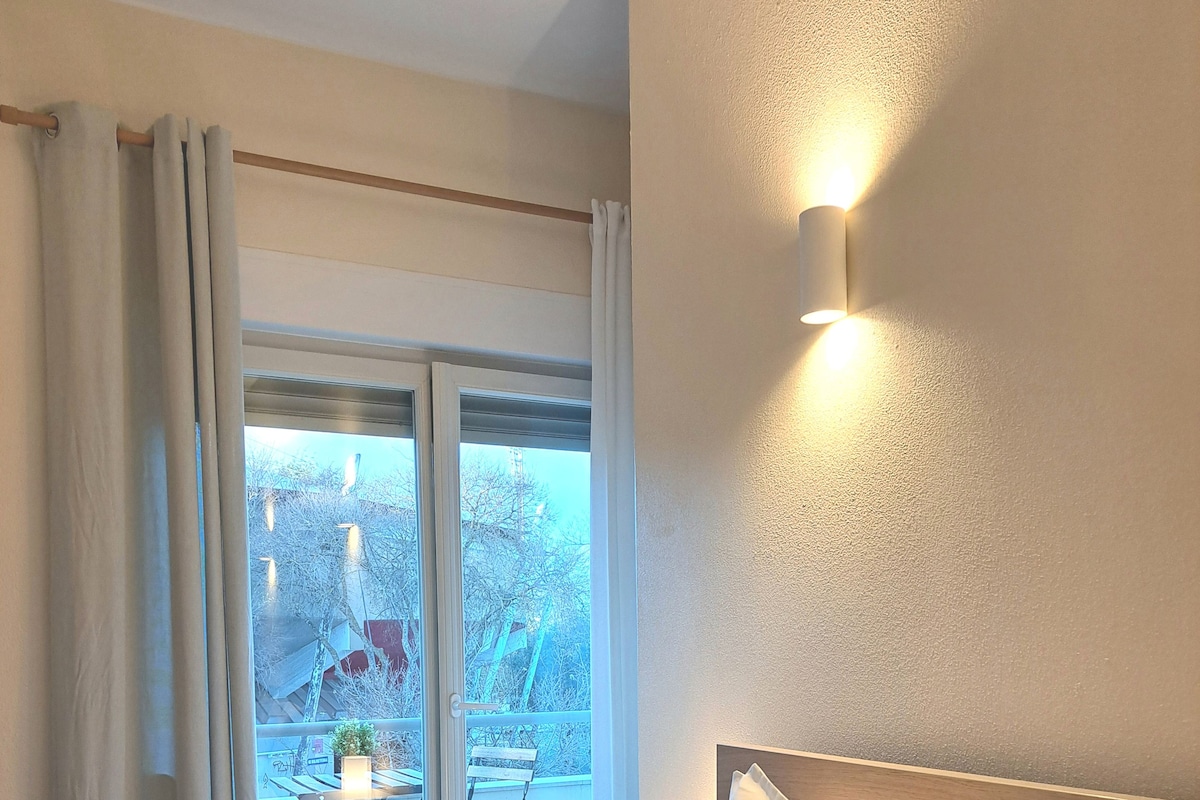 Een hotelkamer met een groot bed, een balkon met een tafel en stoelen, en een wandlamp.