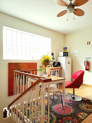 Une pièce avec un escalier en bois, une table à manger avec des chaises, un four à micro-ondes, une chaise rouge, un ventilateur de plafond et un tapis coloré.