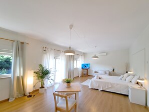 Une pièce moderne et bien éclairée, dotée d’un plancher en bois, d’un lit, d’un canapé, d’une télévision et d’un coin repas avec une table et des chaises.